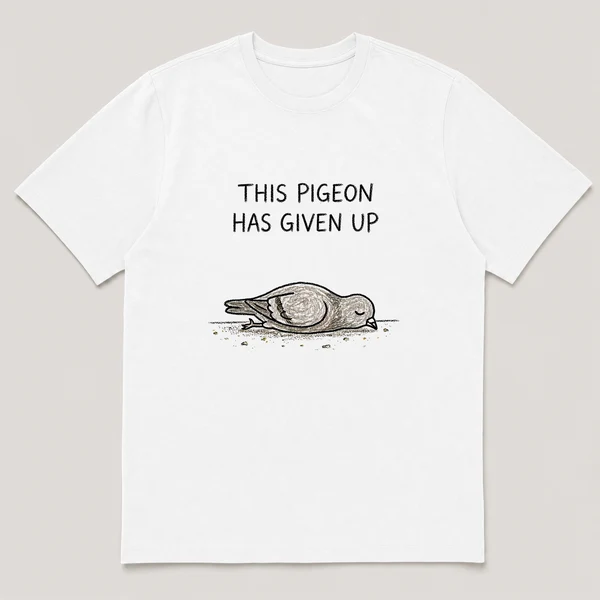 Front view of a White Tee printed with pigeon lies flat on its belly on a sidewalk with crumbs scattered around and the caption THIS PIGEON HAS GIVEN UP